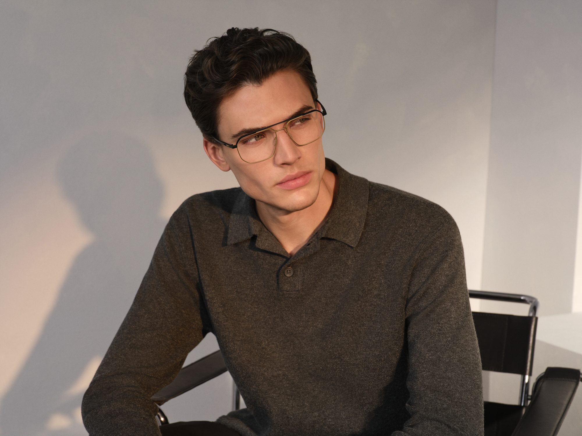 Man in a dark knit polo shirt wearing Rodenstock titanium eyeglasses, seated on a tubular steel chair